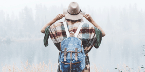 mulher de costas com mochila e chapéu olhando paisagem